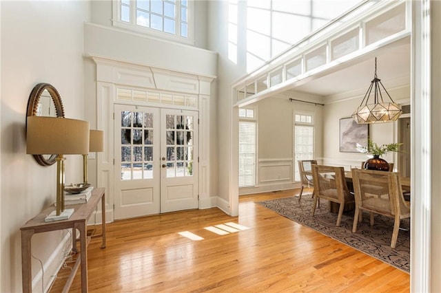 entrance foyer featuring a high ceiling, crown molding, light wood-type flooring, and french doors