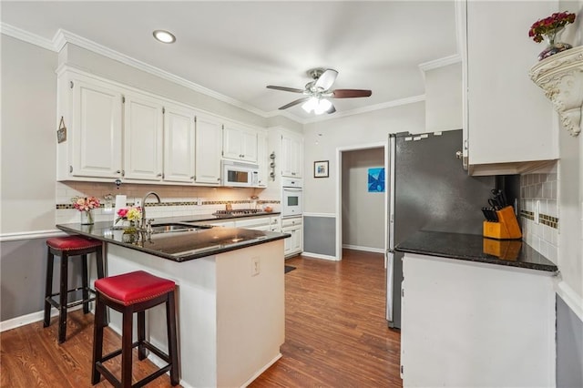 kitchen with white appliances, sink, white cabinets, kitchen peninsula, and backsplash