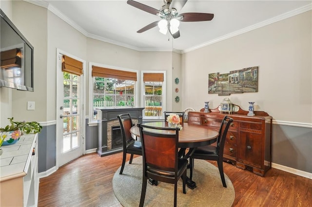 dining area featuring hardwood / wood-style flooring, a stone fireplace, ceiling fan, and crown molding