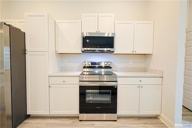 275 Green Commons Dr, Covington, GA 30016 - kitchen featuring stainless steel appliances, light wood-type flooring, white cabinets, and light stone countertops