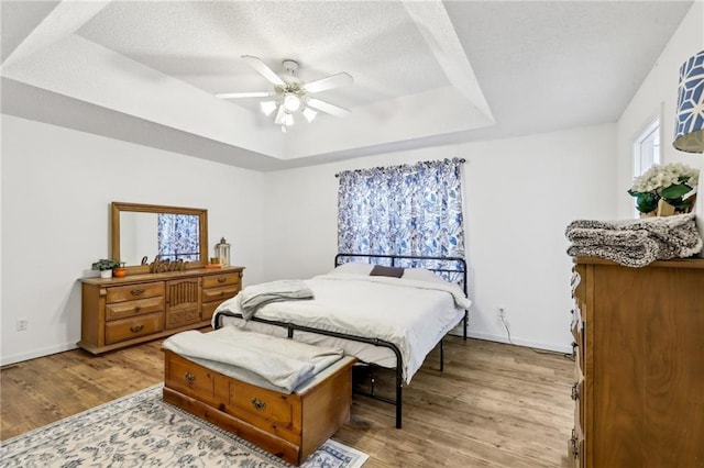 bedroom with ceiling fan, light hardwood / wood-style floors, a raised ceiling, and a textured ceiling