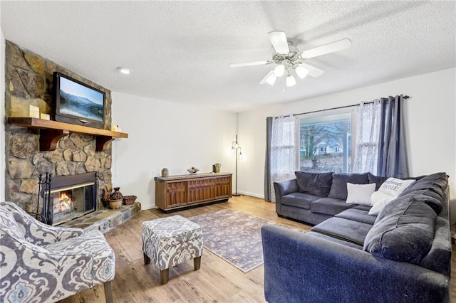 living room featuring ceiling fan, a fireplace, hardwood / wood-style floors, and a textured ceiling