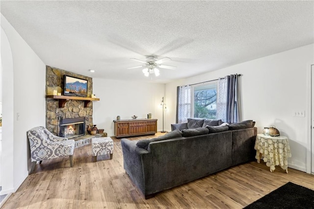 living room featuring hardwood / wood-style flooring, ceiling fan, a fireplace, and a textured ceiling