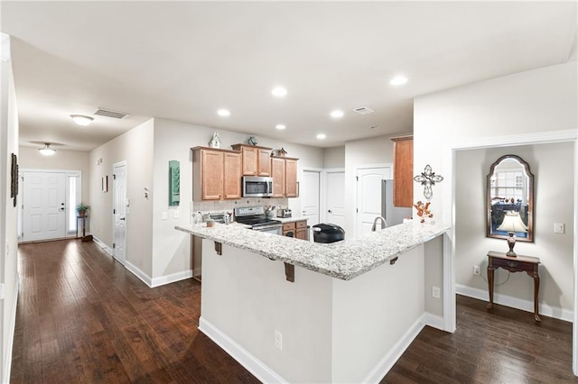 kitchen featuring appliances with stainless steel finishes, a breakfast bar, kitchen peninsula, light stone countertops, and dark wood-type flooring