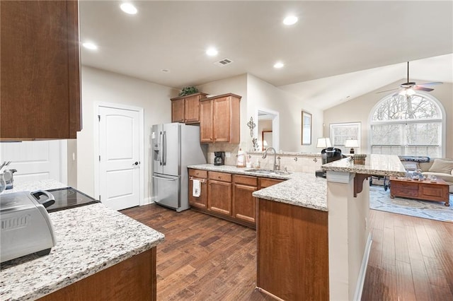 kitchen featuring sink, a breakfast bar area, stainless steel refrigerator with ice dispenser, light stone counters, and kitchen peninsula