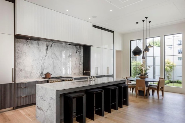 kitchen with sink, decorative light fixtures, an island with sink, and backsplash