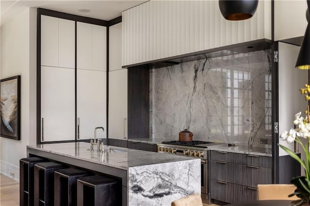 kitchen featuring sink, light stone counters, ventilation hood, light hardwood / wood-style flooring, and a kitchen island with sink