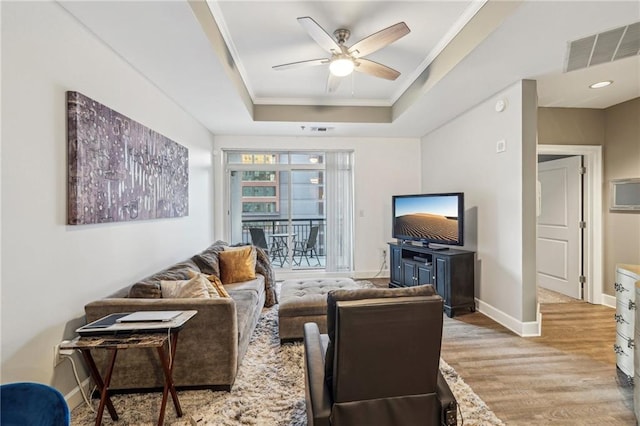 living room with light wood-type flooring, a raised ceiling, ceiling fan, and crown molding