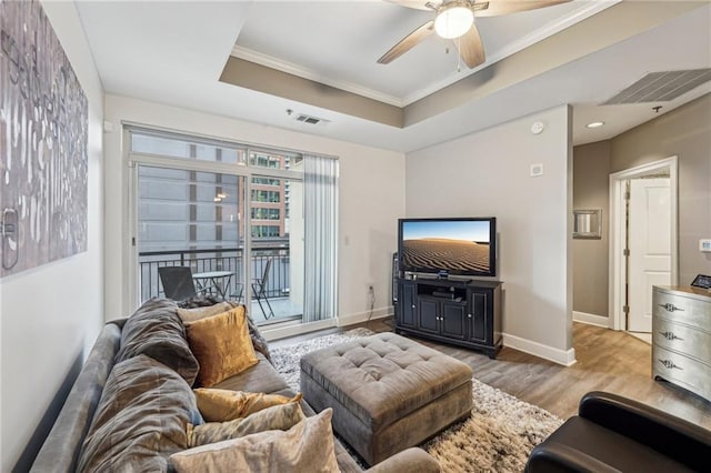 living room with a raised ceiling, ceiling fan, ornamental molding, and light wood-type flooring