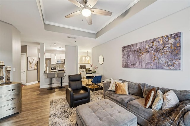 living room featuring hardwood / wood-style flooring, ceiling fan, ornamental molding, and a tray ceiling