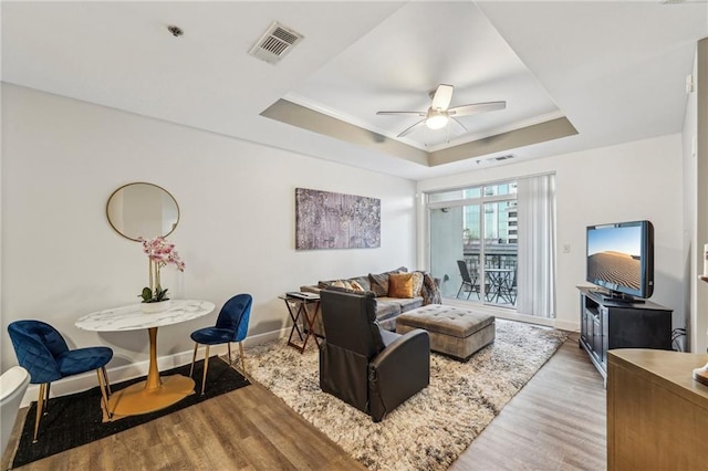 living room featuring a raised ceiling, ceiling fan, light hardwood / wood-style floors, and ornamental molding