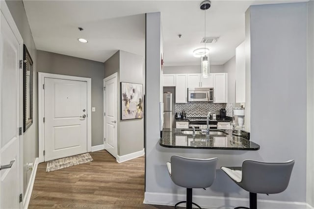 kitchen with dark stone counters, stainless steel appliances, sink, pendant lighting, and white cabinetry