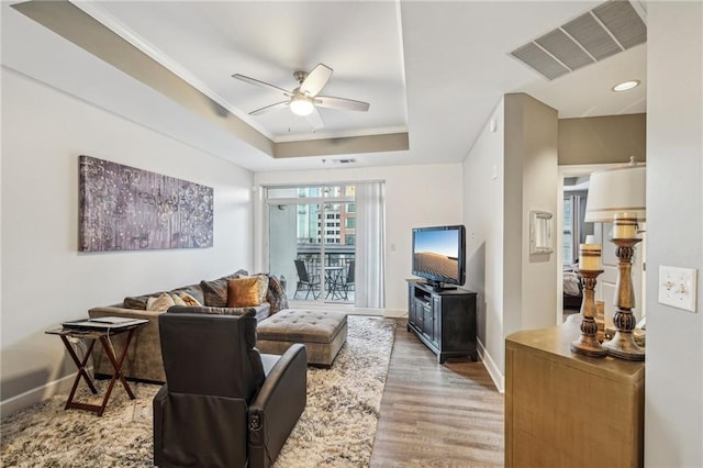 living room with light hardwood / wood-style floors, a raised ceiling, ceiling fan, and crown molding