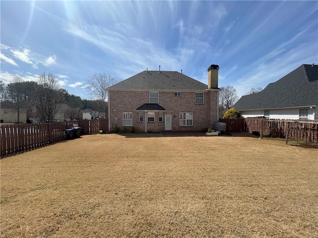 rear view of property featuring a yard, brick siding, a chimney, and fence