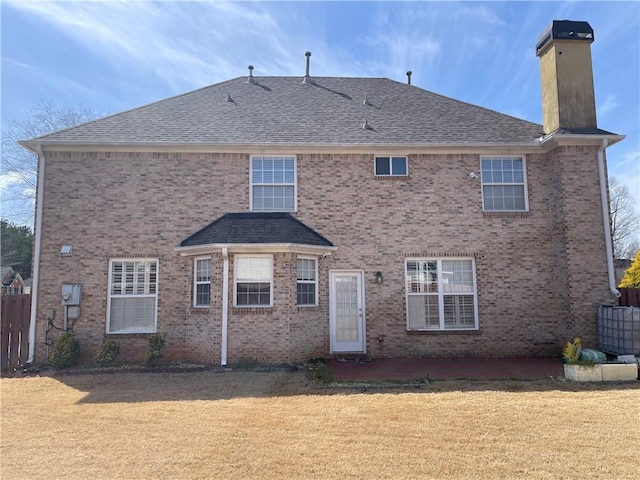 rear view of property featuring brick siding, a yard, a chimney, and fence