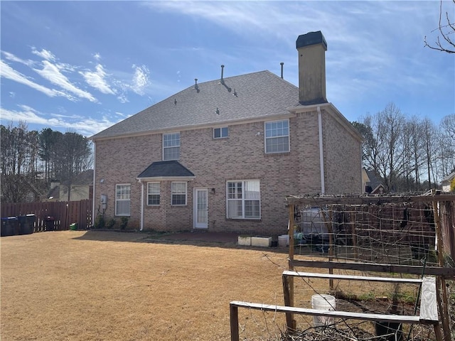 back of house featuring a shingled roof, a lawn, a chimney, fence, and brick siding