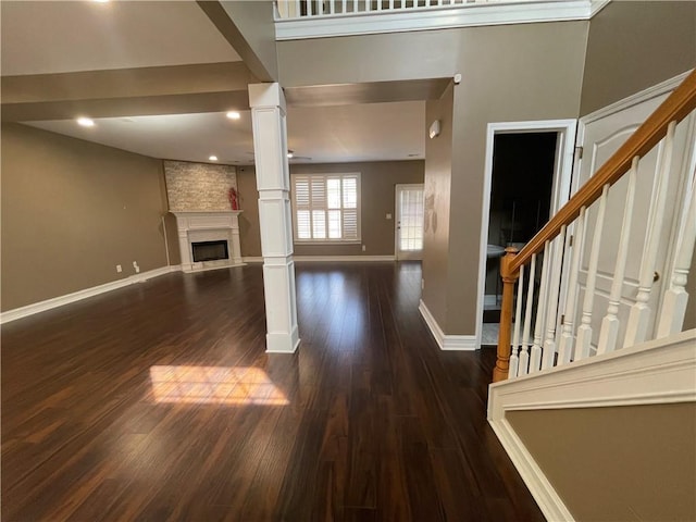 unfurnished living room featuring ornate columns, a large fireplace, wood finished floors, baseboards, and stairs