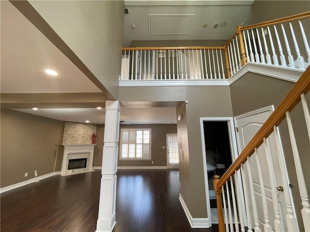 unfurnished living room with ornate columns, a high ceiling, a large fireplace, wood finished floors, and baseboards