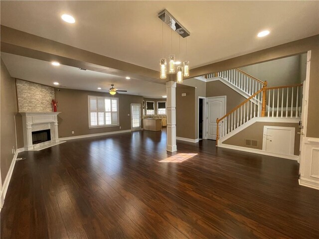 living room featuring decorative columns, ceiling fan, a fireplace, and dark wood-type flooring