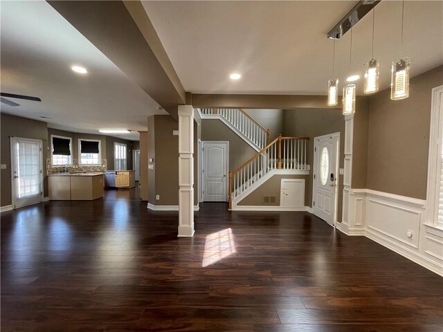 living room with dark hardwood / wood-style flooring, a large fireplace, ceiling fan, and decorative columns