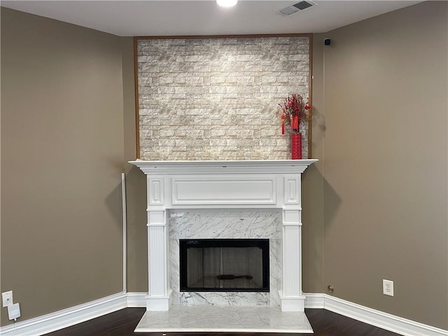 room details featuring visible vents, a fireplace, baseboards, and wood finished floors