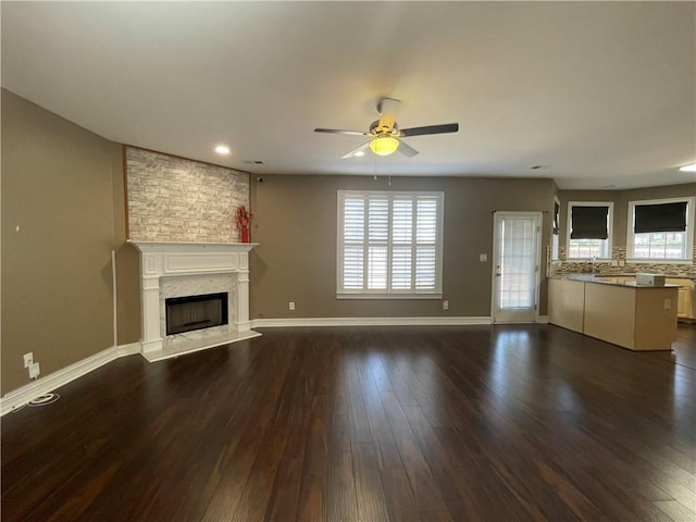 unfurnished living room featuring plenty of natural light, baseboards, dark wood-style flooring, and a high end fireplace