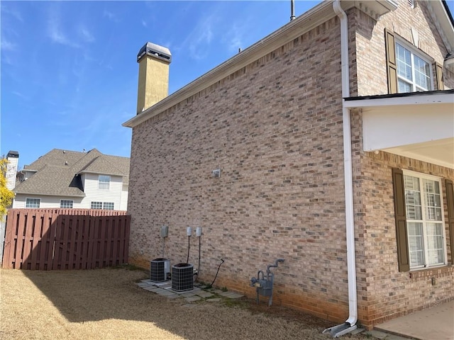 view of property exterior with brick siding, a chimney, and fence