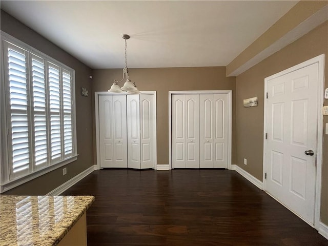 unfurnished dining area featuring a healthy amount of sunlight, dark wood finished floors, and baseboards