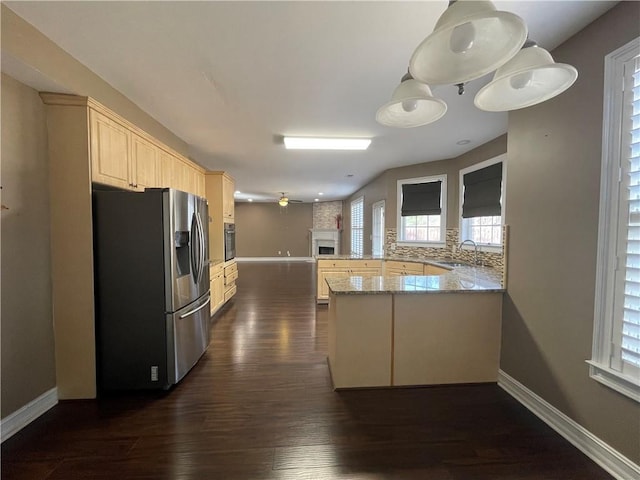 kitchen with light brown cabinets, a peninsula, dark wood-type flooring, a fireplace, and stainless steel refrigerator with ice dispenser