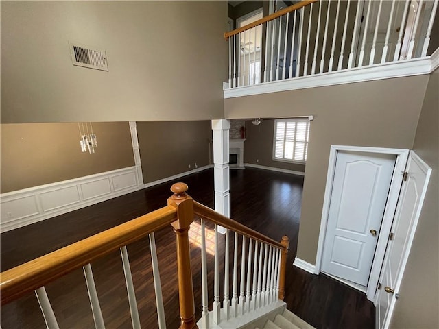 stairway featuring a wainscoted wall, a fireplace, visible vents, a towering ceiling, and wood finished floors