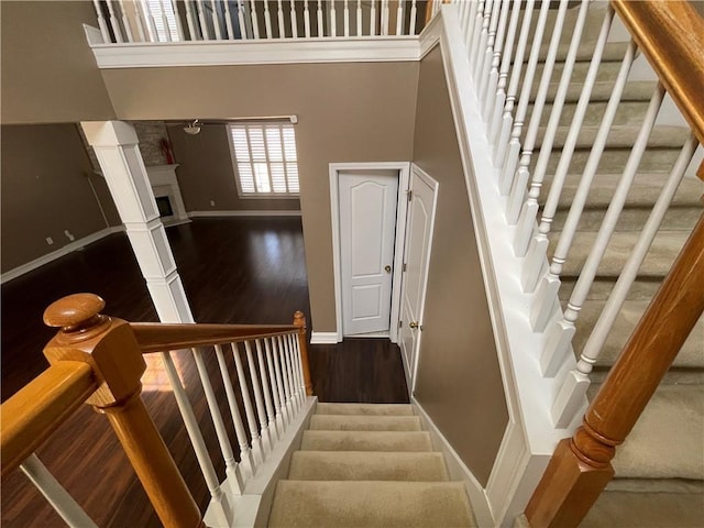 staircase featuring a fireplace, a towering ceiling, baseboards, and wood finished floors