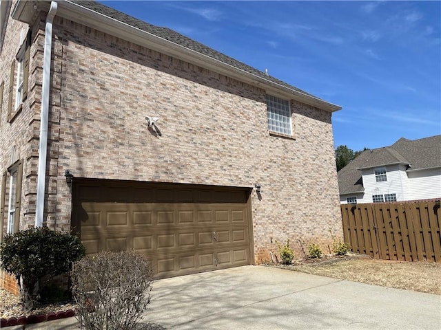 view of property exterior featuring a garage, brick siding, fence, and driveway