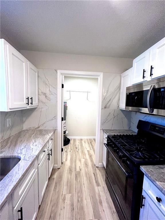 kitchen featuring gas stove, white cabinetry, tasteful backsplash, light stone counters, and light wood-type flooring