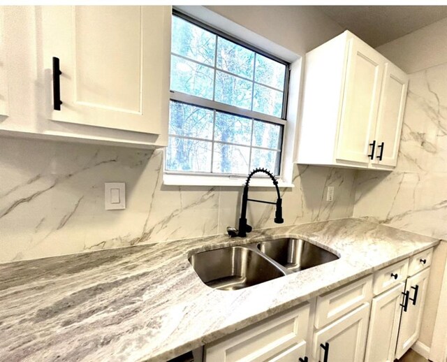 kitchen featuring light stone countertops, backsplash, white cabinetry, and sink