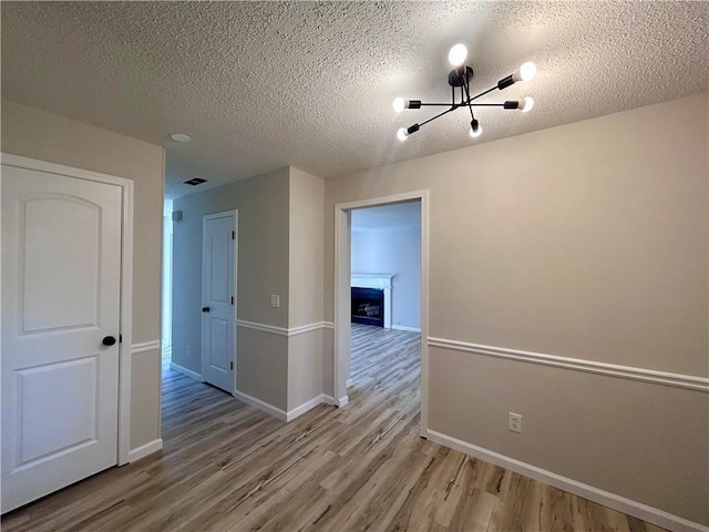 empty room with a textured ceiling, light wood-type flooring, and a notable chandelier