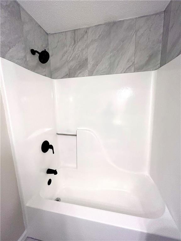 bathroom featuring a textured ceiling and tiled shower / bath