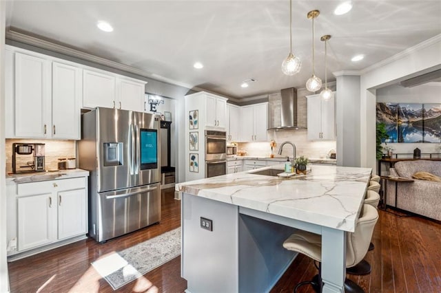 kitchen with appliances with stainless steel finishes, white cabinetry, decorative light fixtures, and wall chimney range hood