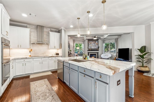 kitchen with white cabinetry, wall chimney range hood, and sink