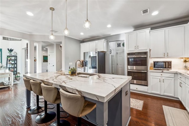 kitchen featuring white cabinets, stainless steel appliances, a center island with sink, and pendant lighting