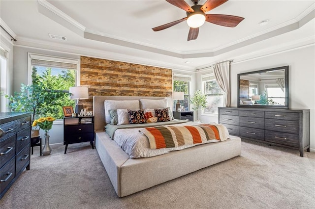 carpeted bedroom featuring wood walls, crown molding, a tray ceiling, and ceiling fan