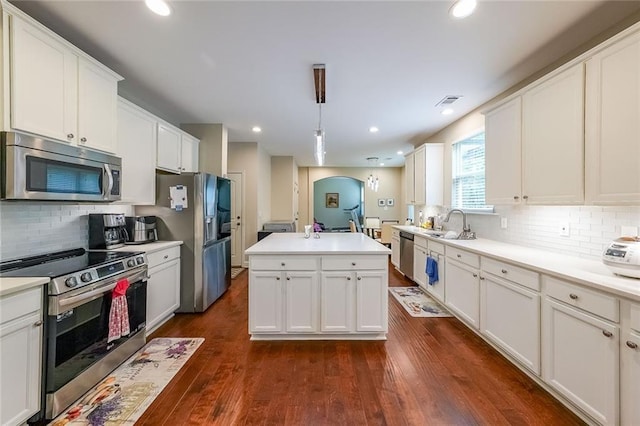 kitchen featuring arched walkways, dark wood-type flooring, white cabinets, appliances with stainless steel finishes, and a center island