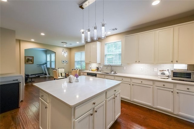 kitchen featuring arched walkways, a sink, visible vents, dark wood-style floors, and tasteful backsplash