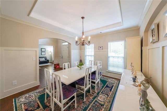 dining room with a wainscoted wall, a tray ceiling, arched walkways, and a decorative wall