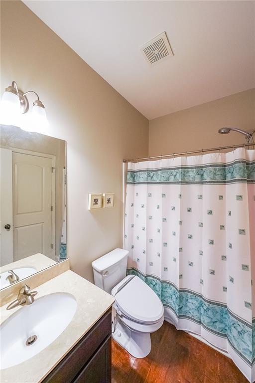 bathroom with lofted ceiling, toilet, wood finished floors, vanity, and visible vents