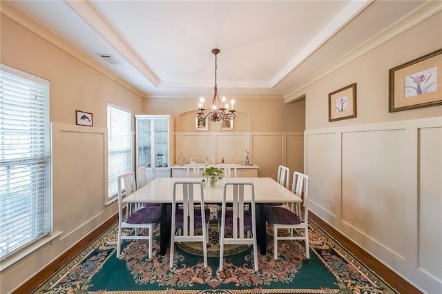 dining area featuring visible vents, a raised ceiling, dark wood finished floors, an inviting chandelier, and a decorative wall