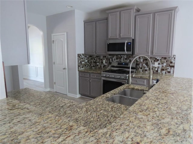 58 Torero Trl, Newnan, GA 30263 - kitchen with appliances with stainless steel finishes, gray cabinets, light stone counters, and arched walkways