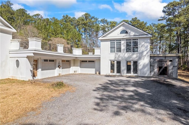 view of front facade featuring french doors, stucco siding, an attached garage, a balcony, and driveway