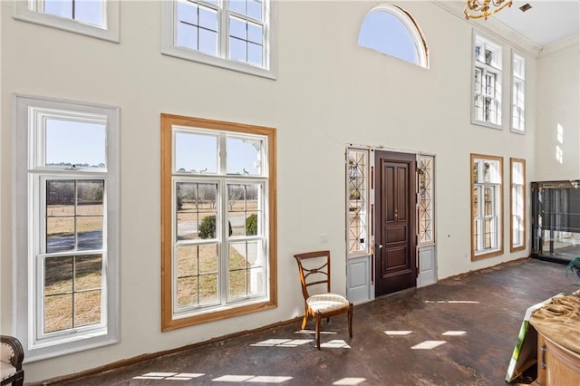 carpeted entryway with a healthy amount of sunlight, crown molding, a towering ceiling, and baseboards