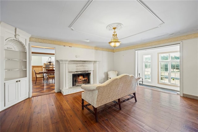 living area with hardwood / wood-style flooring, a brick fireplace, and crown molding