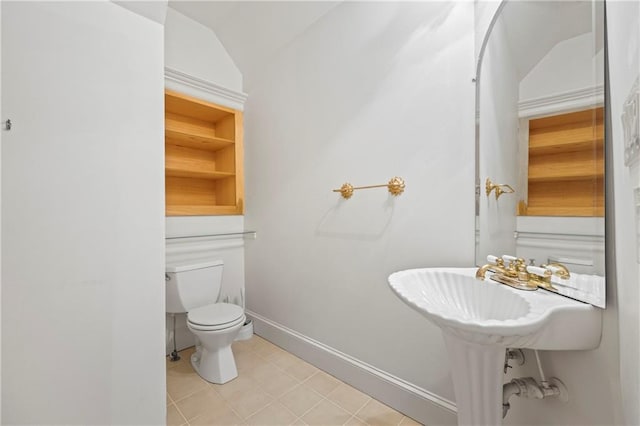 half bath featuring vaulted ceiling, tile patterned flooring, toilet, and baseboards